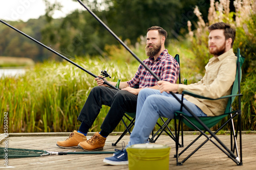 leisure and people concept - happy friends with fishing rods at lake or river