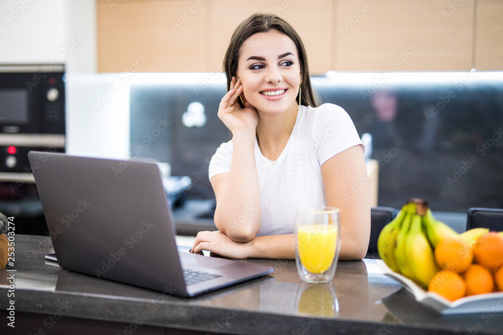 Attractive young woman using laptop and sitting in the kitchen Attractive young woman using laptop and sitting in the kitchen