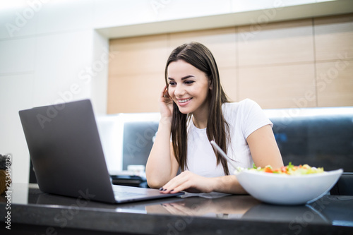 Young prety woman having healthy lunch while working on her notebook photo