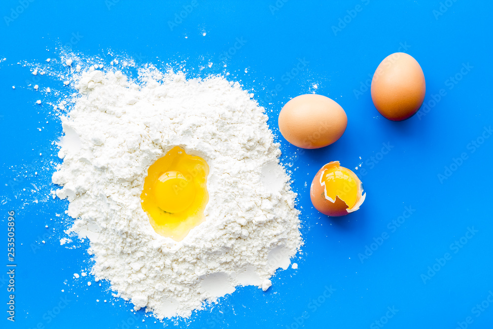 Making dough concept. Pile of flour and eggs on blue background top view Making dough concept. Pile of flour and eggs on blue background top view