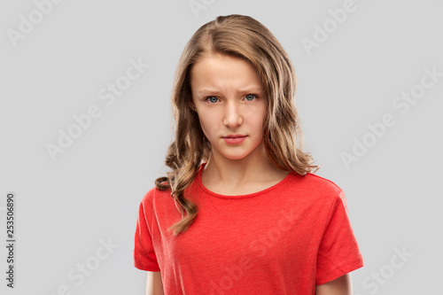 emotion, expression and people concept - sad or angry teenage girl in red t-shirt over grey background