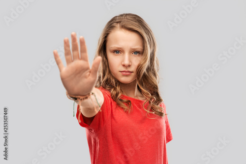 warning, prohibition and people concept - serious teenage girl in blank red t-shirt showing stop gesture over grey background