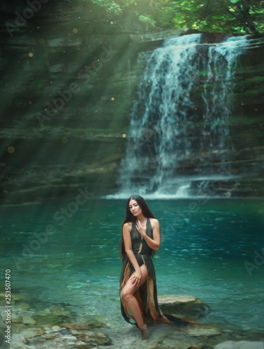 Magic tropical nature, dark-haired sexy girl comes out of the azure transparent clear waterfall lake water, sea nymph in green dress with deep neckline. Mermaid in the sun rays. Art photography