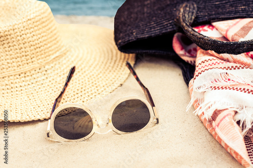 Vintage summer wicker straw beach bag, sun glasses, hat cover-up beachwear wrap on the sand, tropical background.