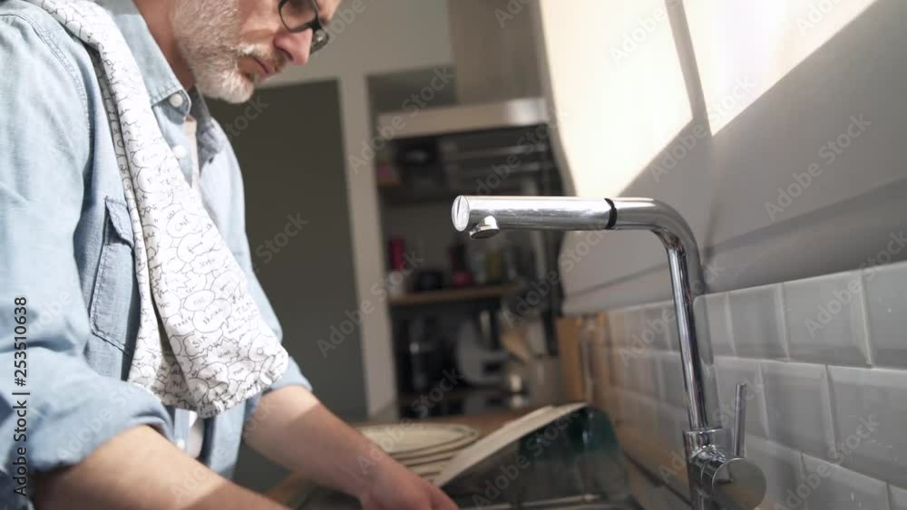 Mature man doing the dishes in sunfilled modern kitchen Mature man doing the dishes in sunfilled modern kitchen