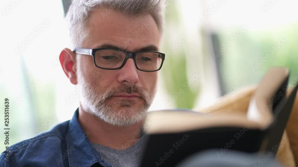 Mature man wearing glasses reading book at home Mature man wearing glasses reading book at home