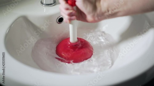 Red and white plunger unblocking white wash hand basin sink, mans hand. photo