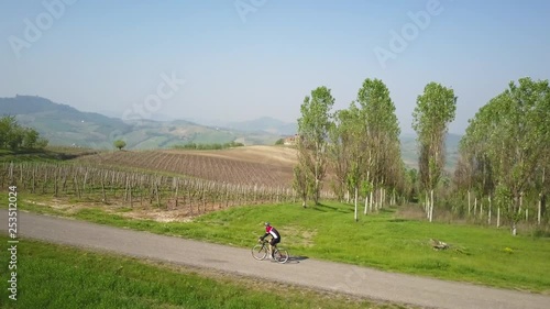 Aerial drone video of a cyclist running on top of the Oltrepò Pavese hills with country landscape as background.