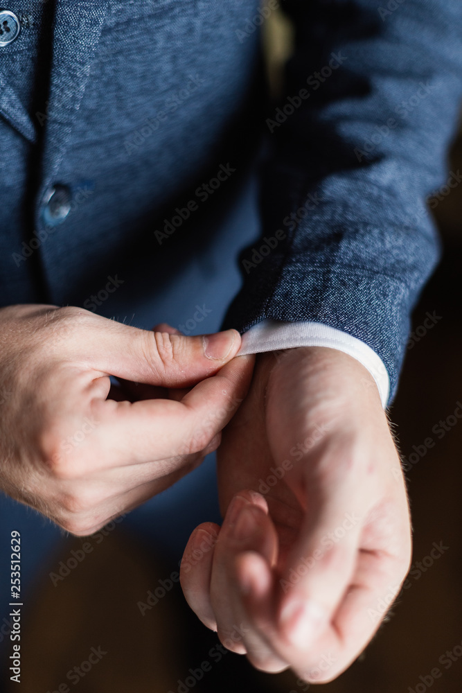 Fototapeta premium Businessman in a white shirt straightens cuffs, standing at the window in natural light. Man buttons cuff-link on French cuffs sleeves luxury white shirt. Concept successfully bisinesman