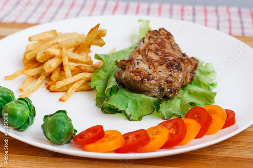 Beefsteak with vegetables and french fries on a white plate
