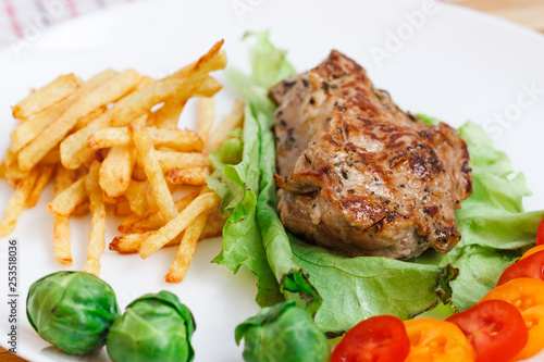 Beefsteak with vegetables and french fries on a white plate