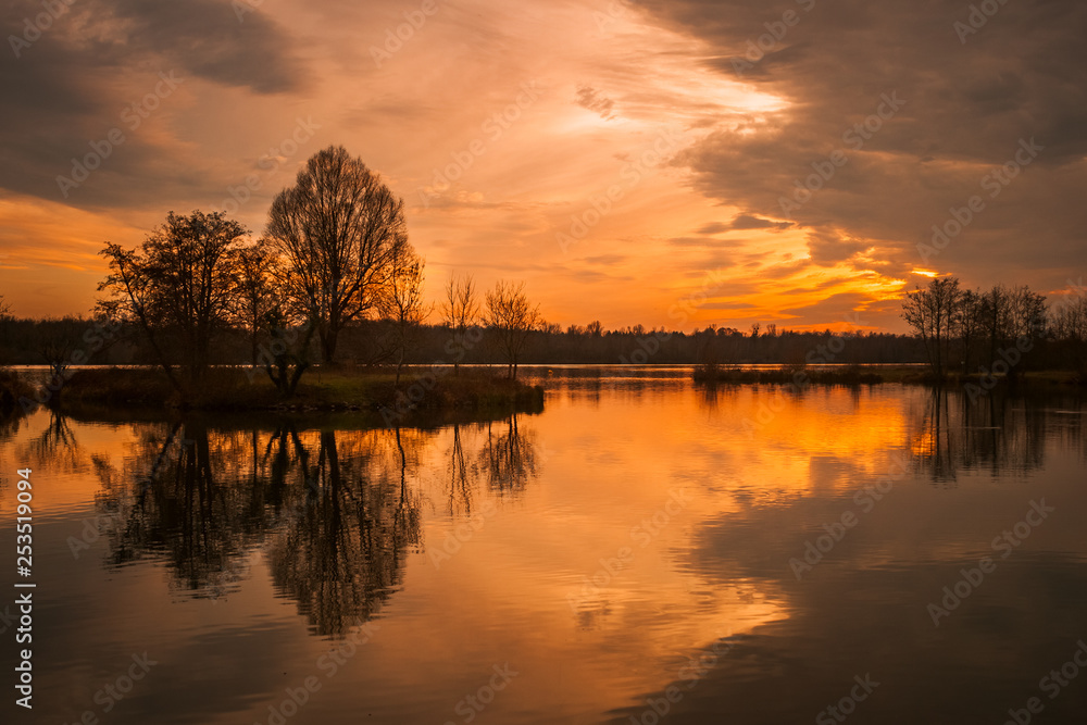 Beautiful landscape of the Rhine River between France and Germany in winter at dusk with sunset colors and dramatic sky. Plobsheim, near Strasbourg, Alsace, France.