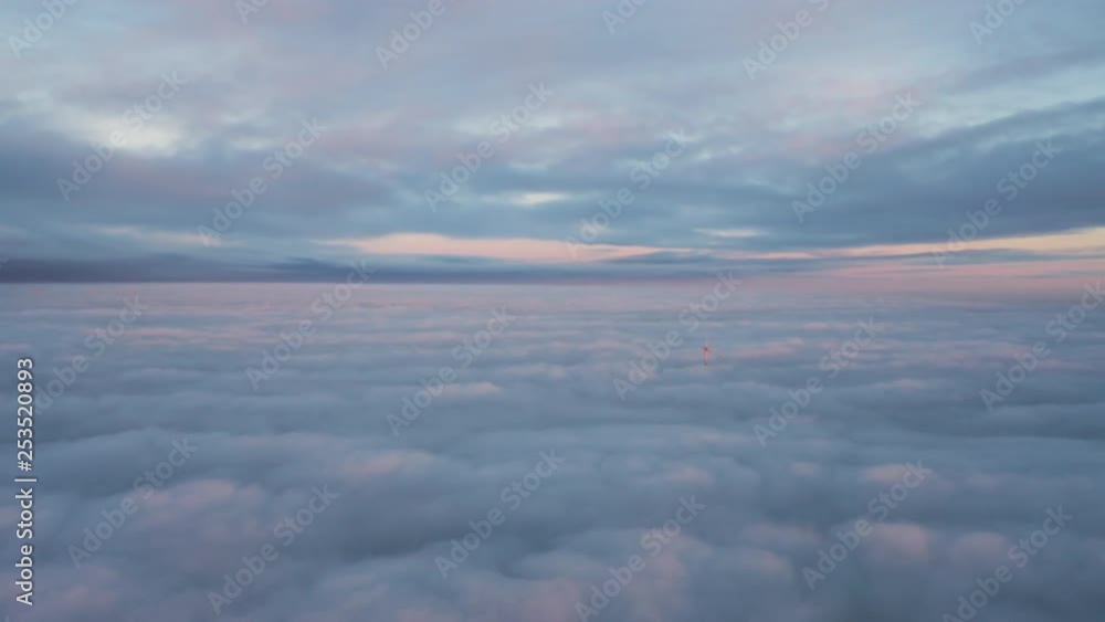 Aerial view above a cloud inversion, rising shot tracking a wind turbine and mountain ranges that are poking through the fluffy clouds. Aerial view above a cloud inversion, rising shot tracking a wind turbine and mountain ranges that are poking through the fluffy clouds.