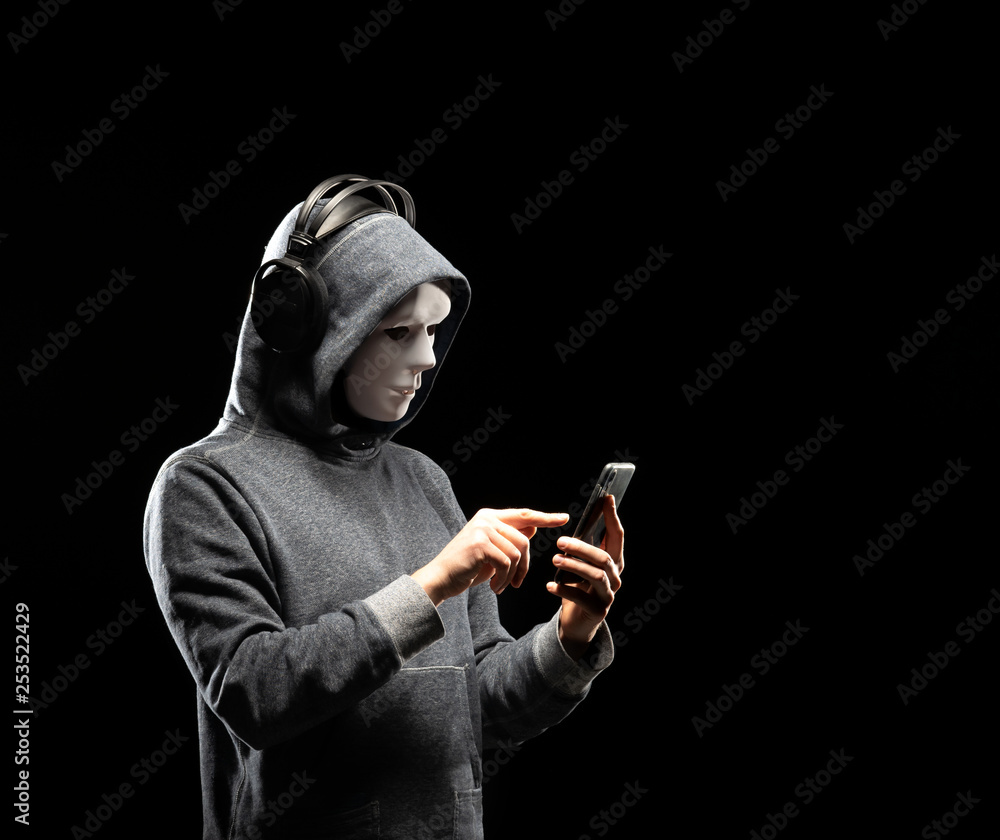 Fototapeta premium Computer hacker in white mask and hoodie. Obscured dark face. Data thief, internet fraud, darknet and cyber security concept.