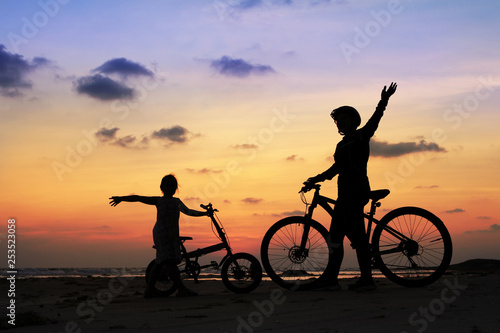 Silhouette of stepmother alone with children and bicycle at sunset so happy