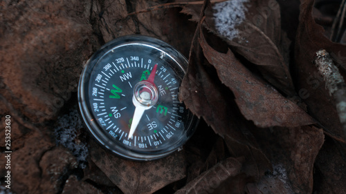 compass with the arrow directed to the north which lies against the background of the dry frozen leaves in the winter in the forest