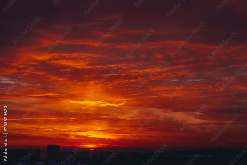 Cityscape with vivid fiery dawn. Amazing warm dramatic cloudy sky above dark silhouettes of city buildings. Orange sunlight. Atmospheric background of sunrise in overcast weather. Copy space. Cityscape with vivid fiery dawn. Amazing warm dramatic cloudy sky above dark silhouettes of city buildings. Orange sunlight. Atmospheric background of sunrise in overcast weather. Copy space.