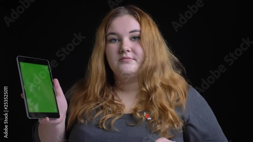 Closeup shoot ofyoung overweight caucasian female using the tablet and showing green screen to camera with background isolated on black photo