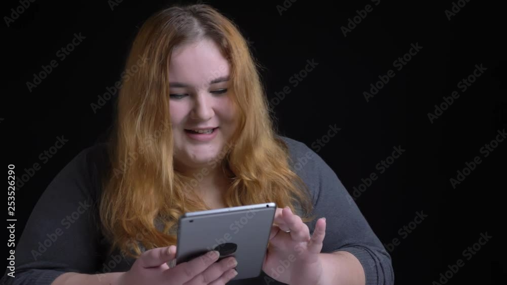 Closeup shoot of young overweight caucasian female typing on the tablet and reacting to social media posts with background isolated on black