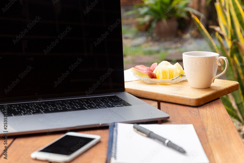 Coffee mug with fresh fruit and laptop on wooden table in the garden. Coffee mug with fresh fruit and laptop on wooden table in the garden.