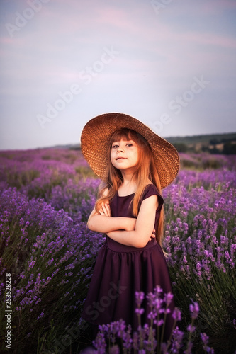 Portrait of smiling child in and straw hat in lavender field in Provence, France. Gorgeous view on Valensole plateau with blooming lavender field around the last week of June.