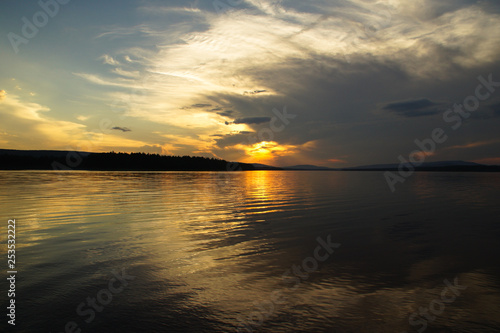 The setting sun shines through the passing thundercloud. Sunset landscape reservoir