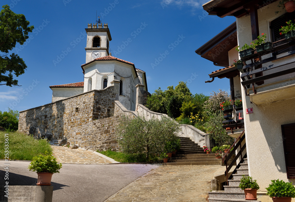 Entrance way to the white stucco catholic church of Saint Leonard with chain and clock belfry in Dolnje Cerovo Gorica Hills Brda Slovenia