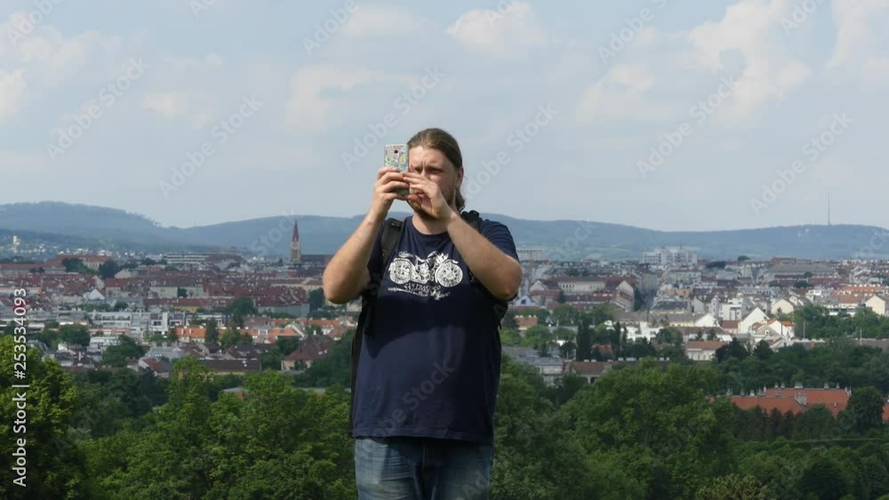 A tourist with a backpack and a scooter takes photos of the panorama of the city. Tourist with backpack on the background of the panorama of the city shoots video on the smartphone. A tourist with a backpack and a scooter takes photos of the panorama of the city. Tourist with backpack on the background of the panorama of the city shoots video on the smartphone.