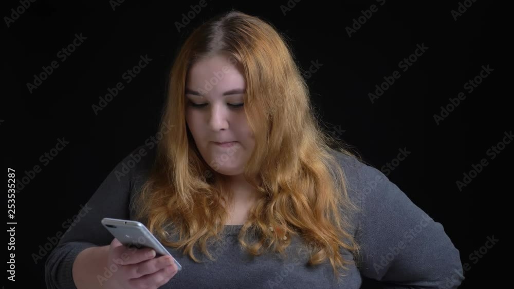 Closeup shoot of young overweight caucasian female browsing on the phone and reacting top social media posts then looking at camera and smiling Closeup shoot of young overweight caucasian female browsing on the phone and reacting top social media posts then looking at camera and smiling