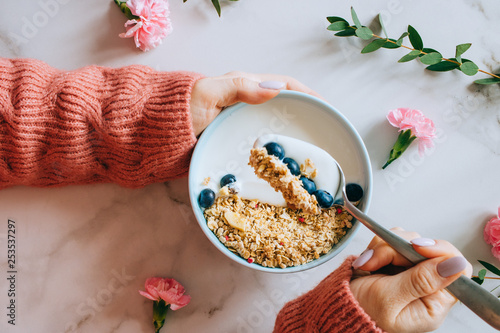 Woman in coral woolen sweater eating breakfast bowl with muesli and yogurt, berries and hazelnuts. Clean eating, vegetarian, vegan, alkiline diet food concept photo