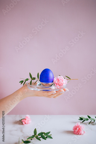 The girl is holding a violet easter egg on a stand, pink and marble background, minimalism, flowers