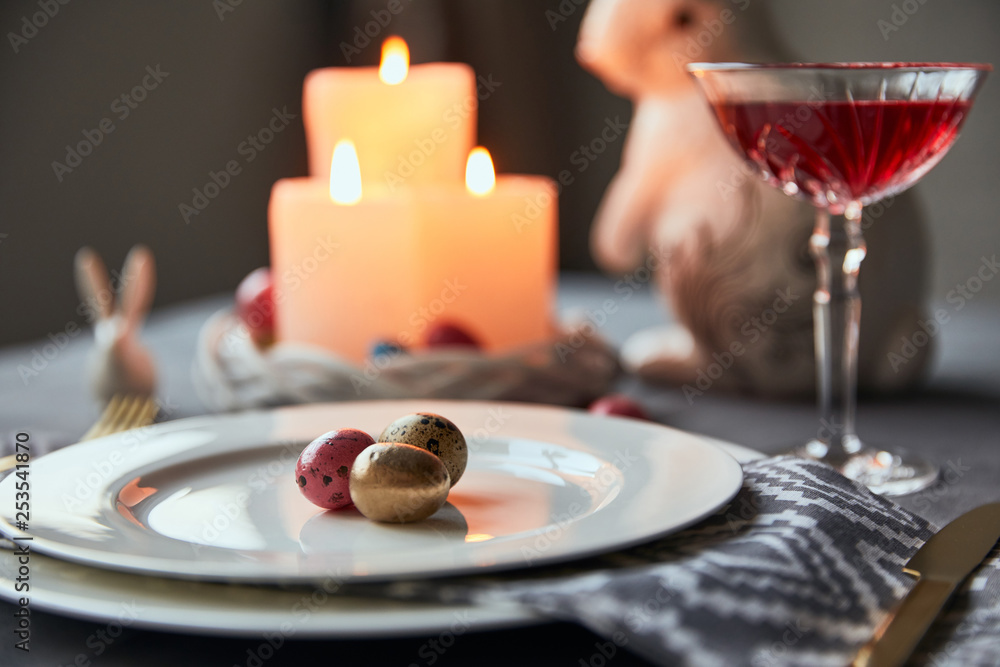 selective focus of plates with eggs, wine in crystal glass, burning candles and decorative bunnies on table at home