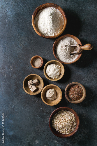 Ingredients for baking bread. Variety of wheat and rye flour, grains, yeast, sourdough over dark blue texture background. Flat lay, space