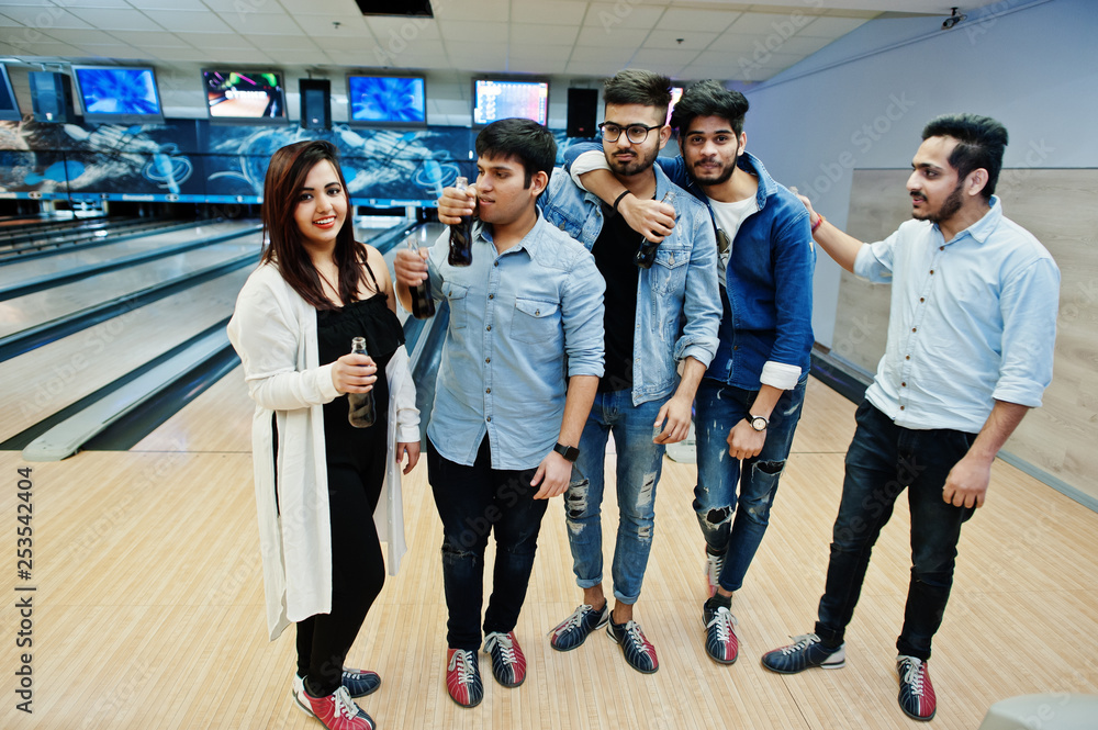Group of five south asian peoples having rest and fun at bowling club. Holding cold soda drinks from glass bottles.