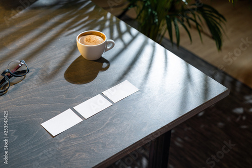 Close up of coffee cup, glasses and business cards on dark wooden table.