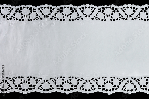 White paper lace doily, closeup on black background.