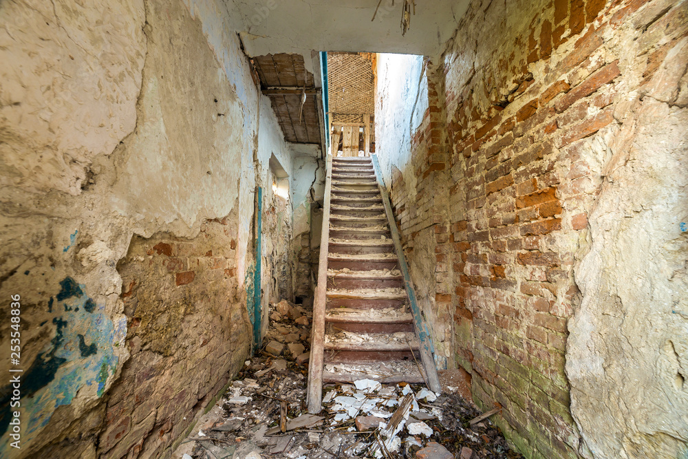 Large spacious forsaken empty basement passageway of ancient building or palace with cracked plastered brick walls and narrow steep wooden staircase ladder.