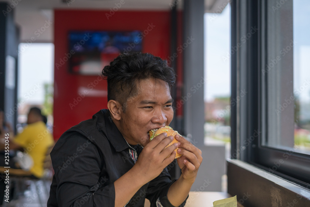 a handsome man having or eating burger with face expression at restaurant a handsome man having or eating burger with face expression at restaurant