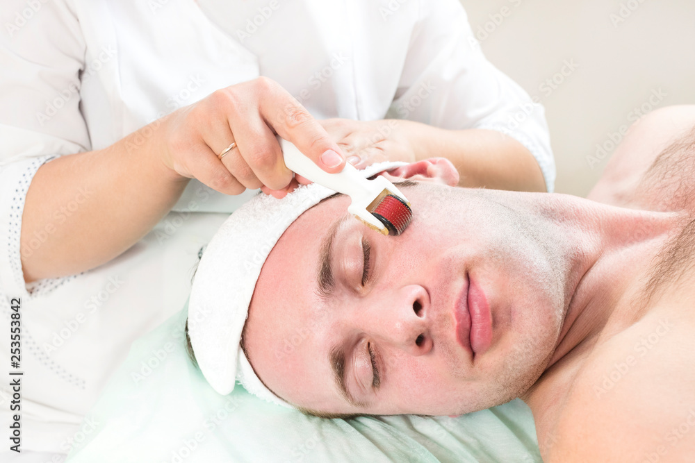 The man undergoes the procedure of medical micro needle therapy with a modern medical instrument derma roller. 