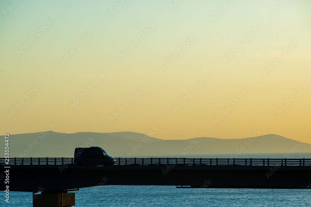 Cars on the highway bridge during the dawn against the backdrop of mountains and the sea