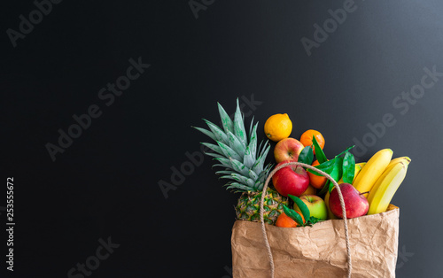 fresh healthy organic fruits bought on weekly market in brown paper bag against dark table background