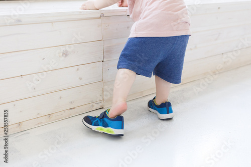 Сute little toddler learn to dress shoes while leaning on the wooden podium. Сoncept of caring for kids