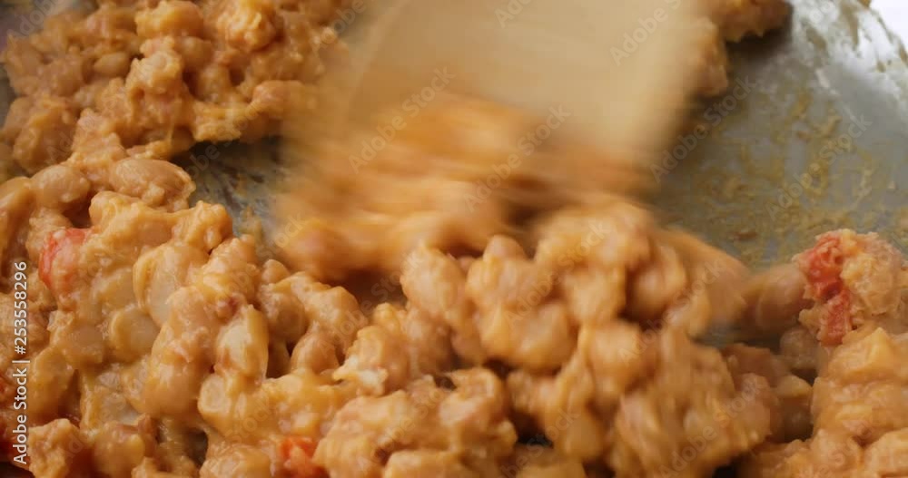 Close video of baked beans with bacon in a tomato sauce being stirred in a skillet while heating with a wood spoon illuminated with natural lighting. Close video of baked beans with bacon in a tomato sauce being stirred in a skillet while heating with a wood spoon illuminated with natural lighting.