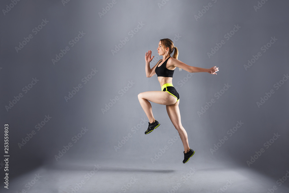Fototapeta premium Side view tightened fit beautiful athlete jumps in a sports suit during cardio exercise. Concert of endurance and fat burning