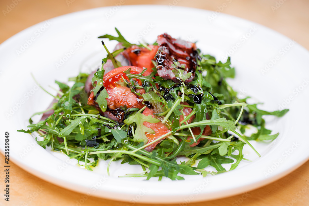 Salad with pieces of marbled beef and arugula on a white plate Salad with pieces of marbled beef and arugula on a white plate