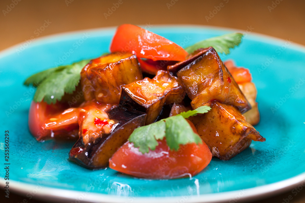 Salad of tomatoes and fried eggplant with sauce on blue plate Salad of tomatoes and fried eggplant with sauce on blue plate