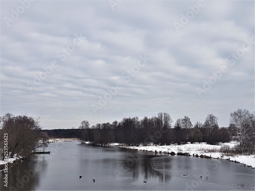 Winter river and snow against a blue sky with clouds. © Konstantin