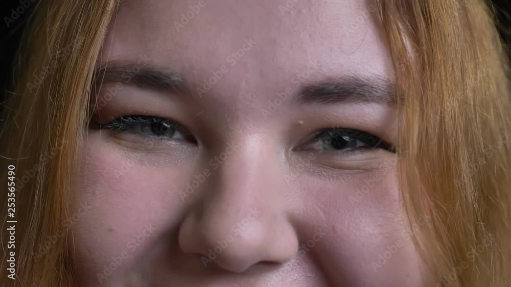Closeup shoot of young overweight female face with gray eyes looking straight at camera with smiling cheerful facial expression Closeup shoot of young overweight female face with gray eyes looking straight at camera with smiling cheerful facial expression