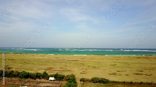 aerial view by drone, rising from small hut and looking out over field towards the beach and sea in the distance in Kaliantan