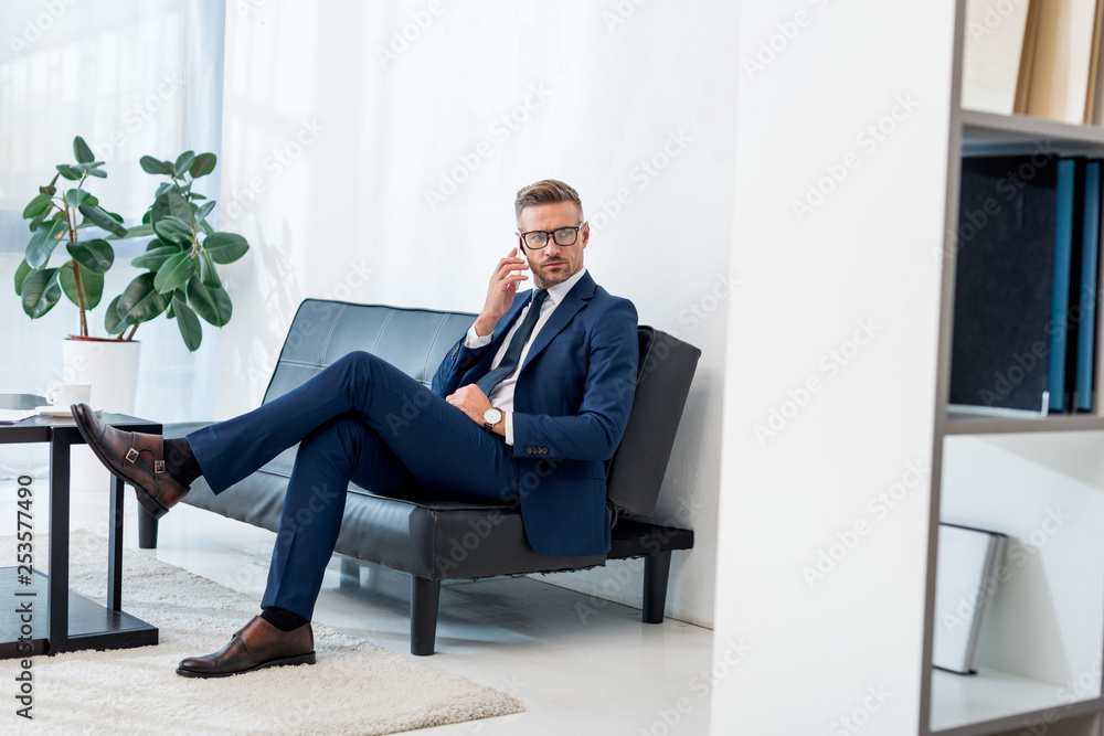 handsome businessman in glasses sitting on sofa and talking on smartphone handsome businessman in glasses sitting on sofa and talking on smartphone